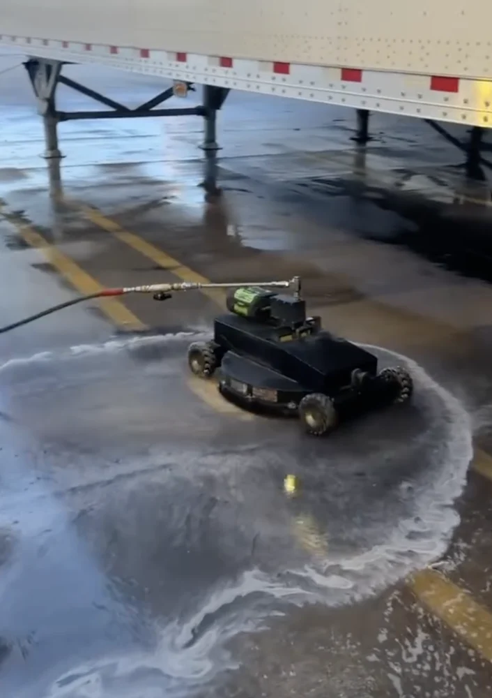Robotic surface cleaner working on concrete beside a loading trailer