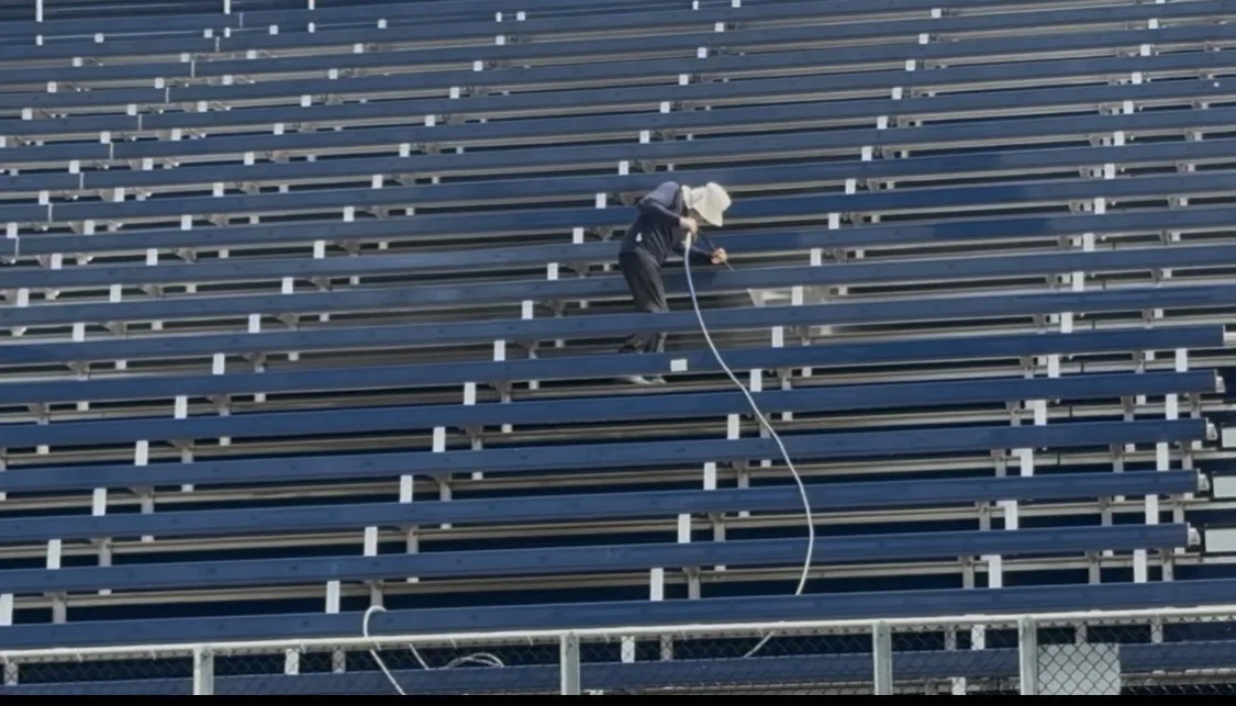 Pressure Kleen technician using cleaning equipment among the blue stadium bleachers