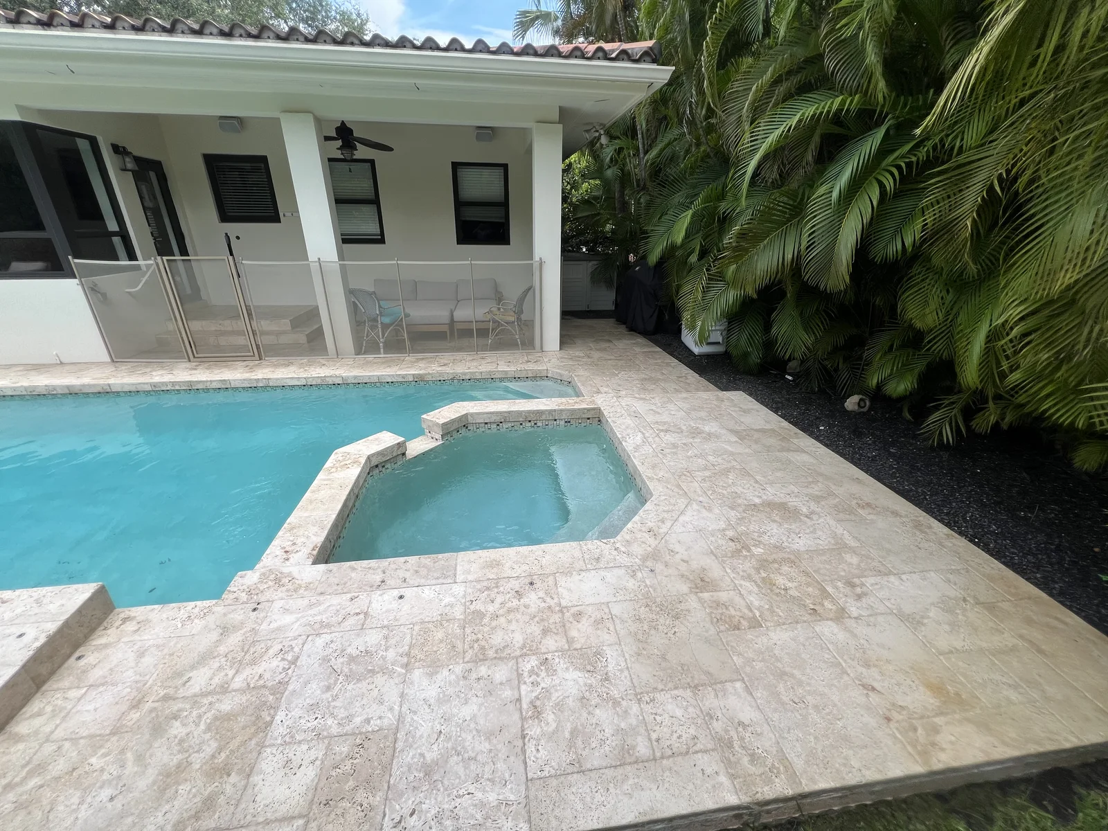 Light-colored residential pool deck surrounding a swimming pool and spa beside a covered patio
